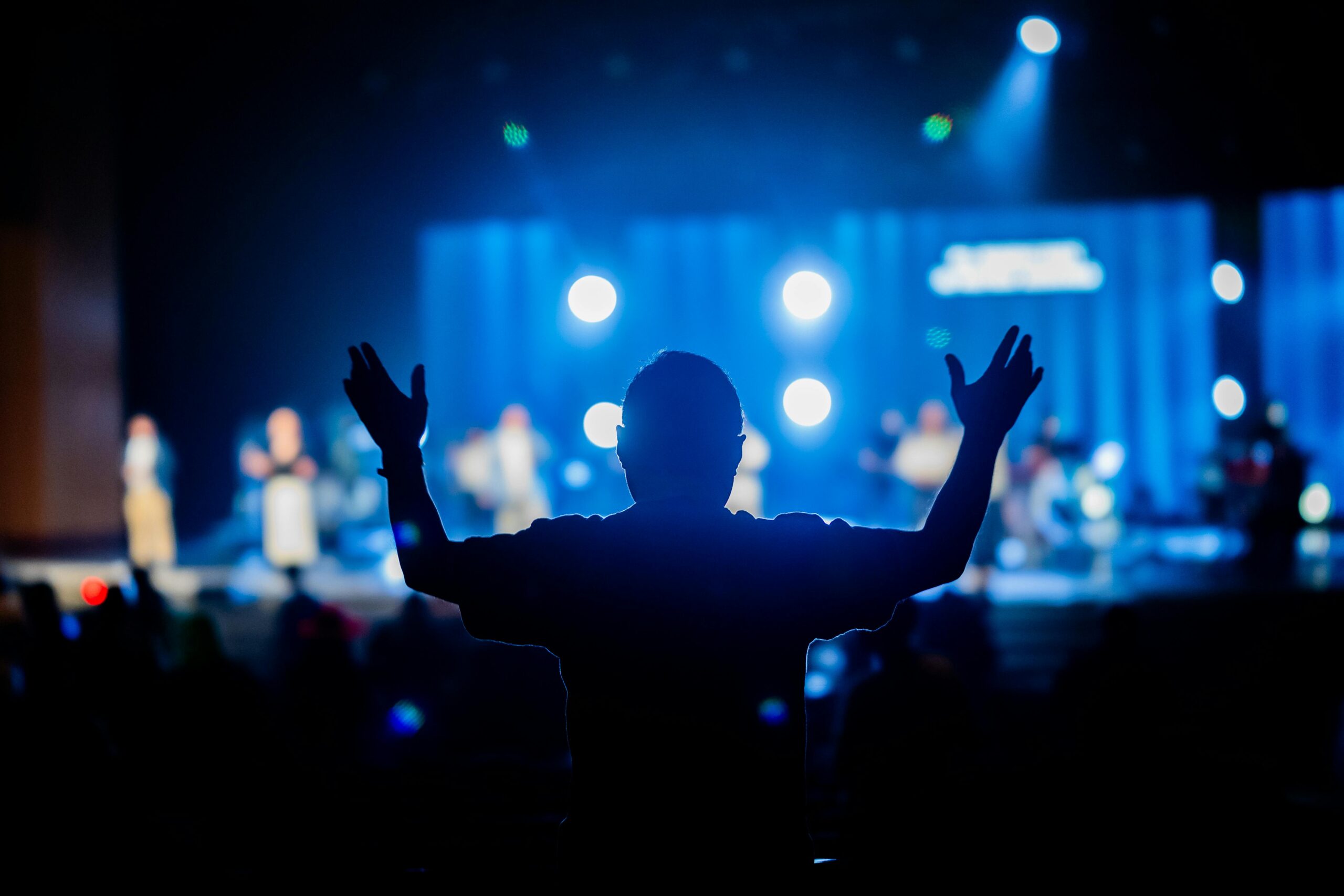About Silhouette of a person with raised hands at a vibrant concert stage.