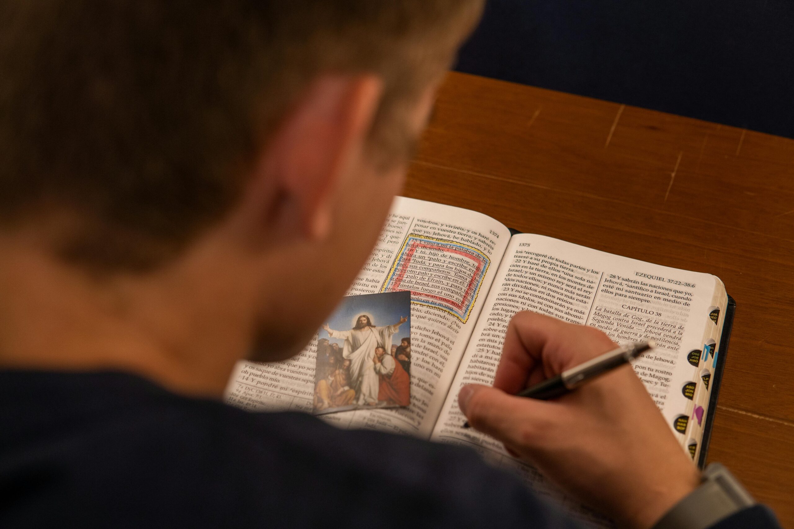 About A person makes notes while reading a Bible with a photo of Jesus, focusing on study and faith.